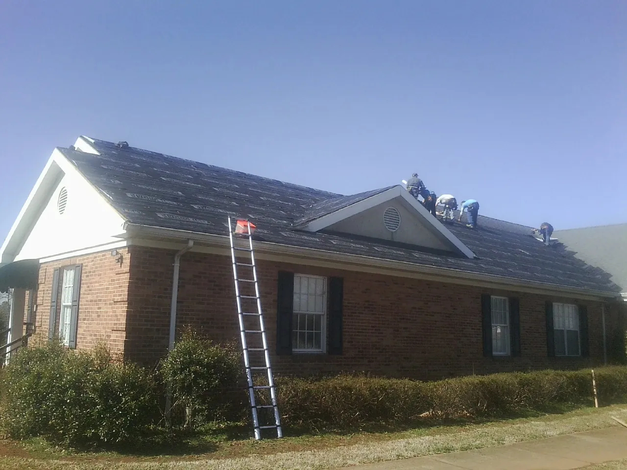 Crew tearing shingles off a brick ranch roof with a ladder set — Metal Roof Repair work by our crew in Pickerington