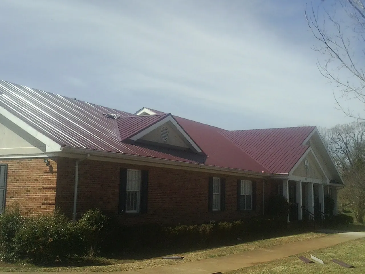 Red metal roof with gabled entries on a long brick building, from a Hail Damage Roof Repair job in Pickerington