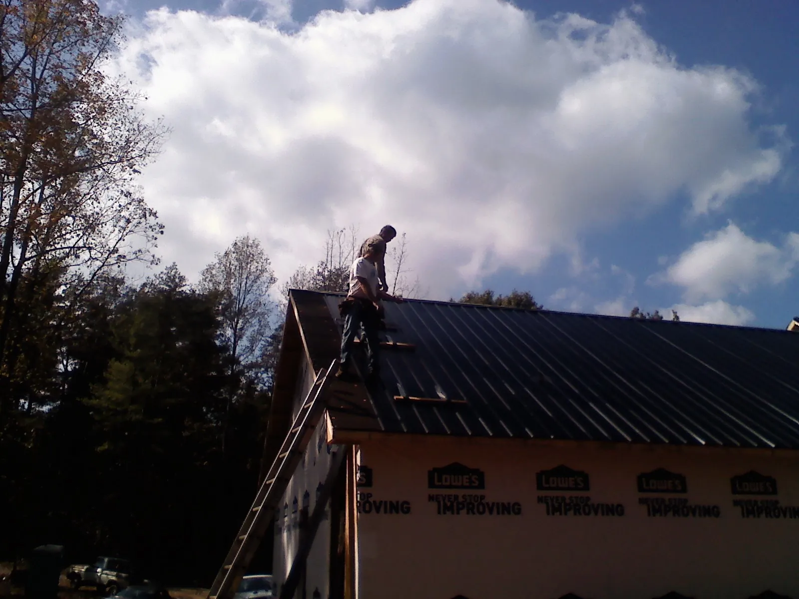 Roofer fastening dark metal panels high against a cloudy sky, from a Roof Inspection job in Pickerington